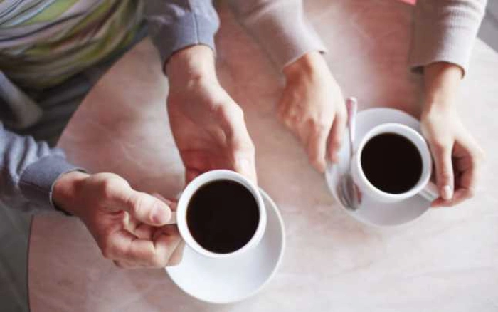 maini ce tin doua cesti de cafea neagra pe o masa