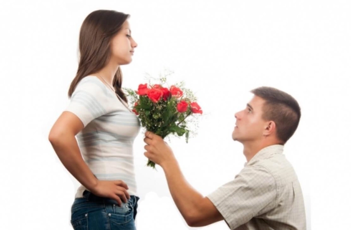 un barbat care sta in genunchi cu un buchet de flori in mana si priveste o fata