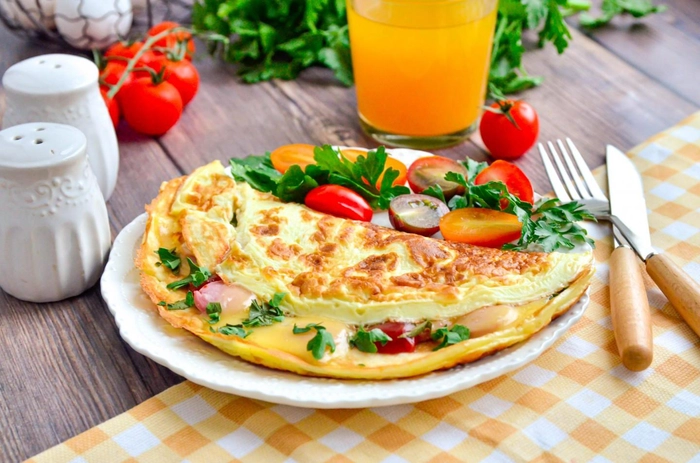omleta cu legume langa un pahar cu suc, condimente si tacamuri pe o masa