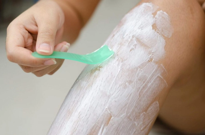 femeie care indeparteaza cu o spatula crema pentru epilare de pe picioare
