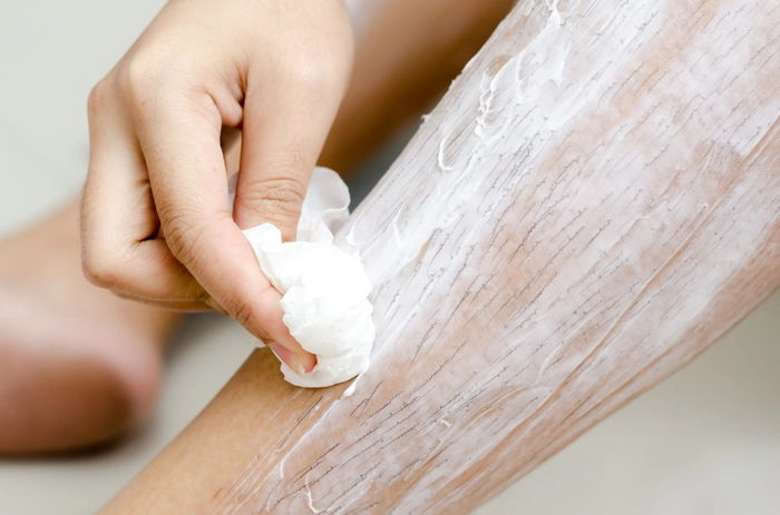 femeie care indeparteaza cu o spatula crema pentru epilare de pe picioare
