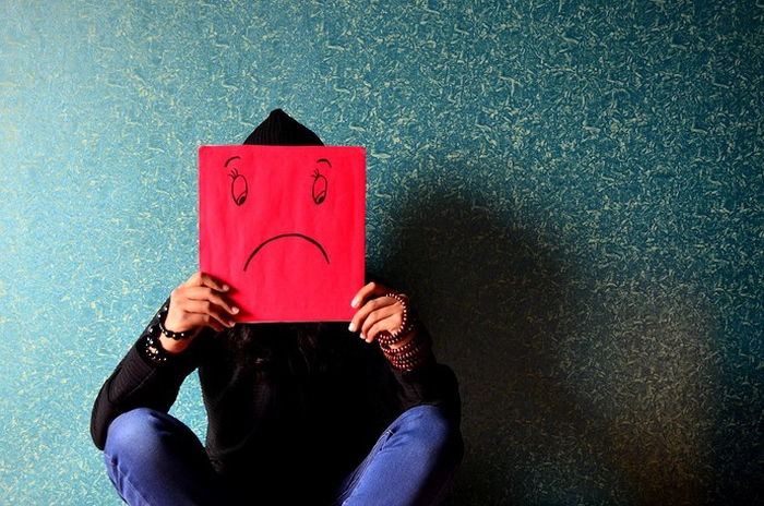 depresia reprezentată de un bărbat care ține în mâini un panou roșu cu o față tristă