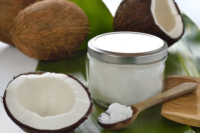 un cocos taiat in doua langa o lingura cu ulei de cocos si un recipient cu ulei de cocos