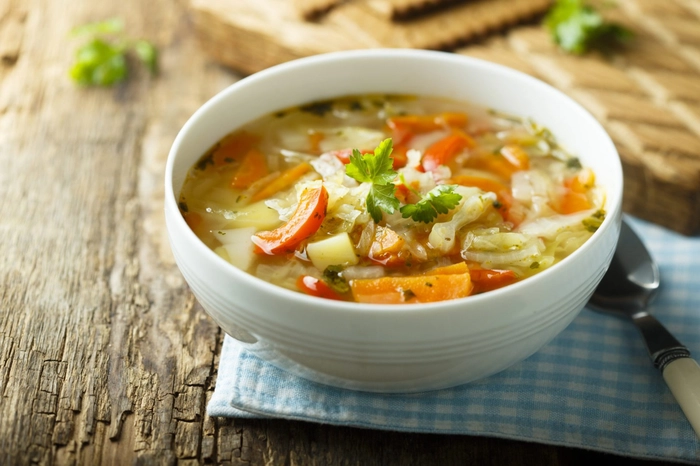 bol ciorba de carne cu legume, prezentat pe un platou de lemn