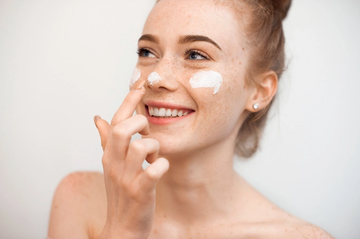 femeie care aplica o crema pentru pete pe fata si zambeste