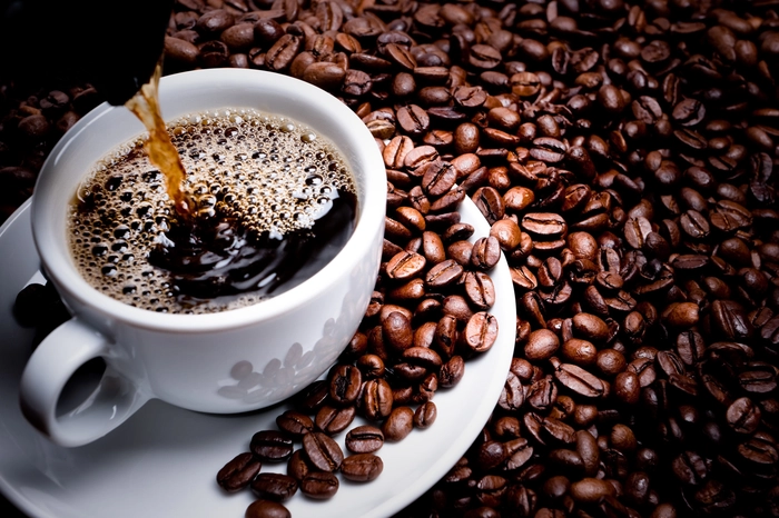 cafea turnata in ceasca langa boabe de cafea
