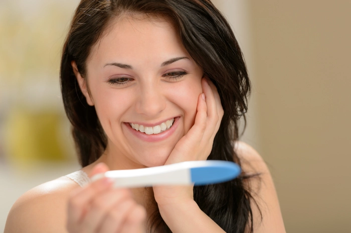 femeie care priveste un test de sarcina si zambeste