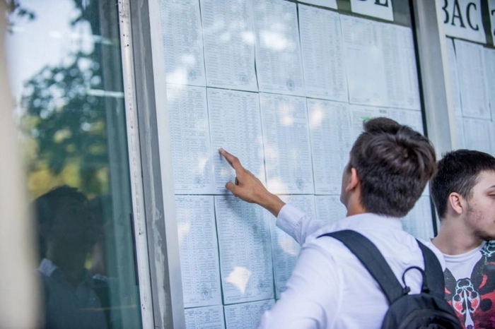 Baieti in fata afisierului, unul dintre ei atingandu-l cu degetul