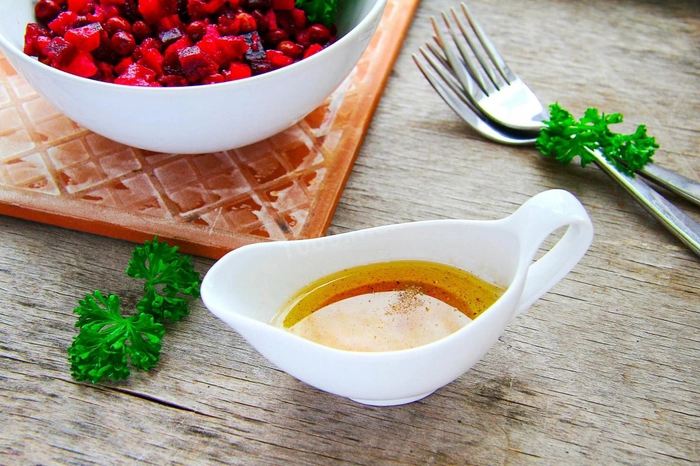 un recipient pe o masa cu sos vinegrette langa un bol cu salata si doua furculite