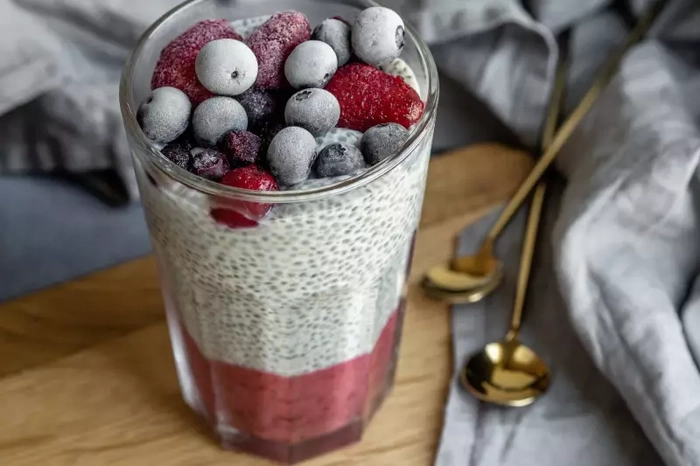 seminte de chia cu iaurt si fructe intr-un pahar alaturi de un servetel si doua lingurite
