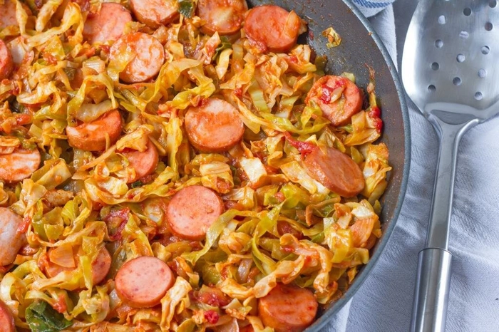 varza calita cu carnati pe o farfurie langa o lingura de fier