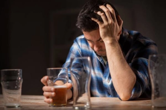 barbat care isi reazama capul cu o mana, iar in cealalta mana tine un pahar cu alcool
