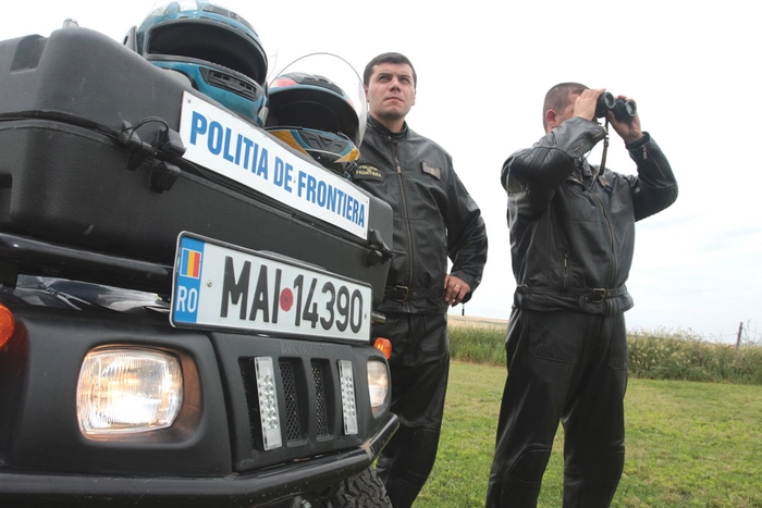  Doi barbati ce poarta uniformele Politiei de Frontiera, langa o masina ce apartinei aceleiasi institutii