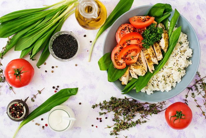 un bol cu salata pe o masa inconjurat de mai multe alimente
