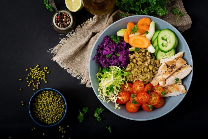 un bol cu salata pe o masa inconjurata de mai multe ingrediente