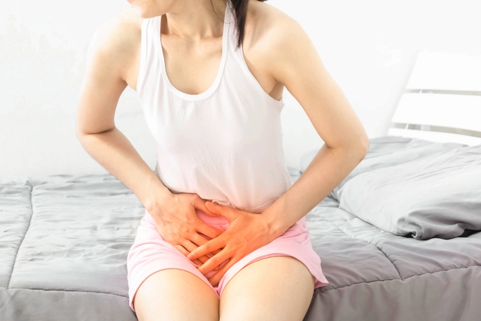 grafica femeie care sta asezata pe pat si se tine de burta din cauza infectiei urinare