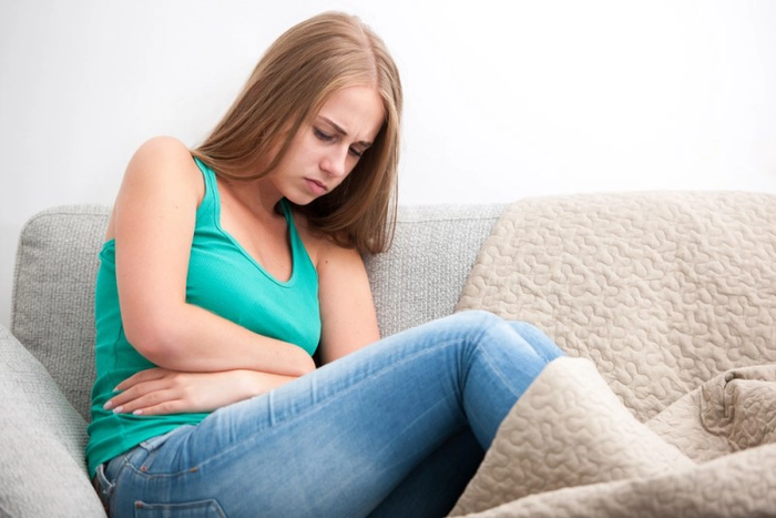 femeie asezata pe pat care se tine de abdomen din cauza menstruatiei