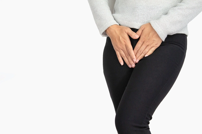 o femeie îmbrăcată cu pantaloni negri care își ascunde zona intimă