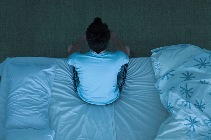 barbat care sta asezat pe pat noaptea si sufera de insomnie