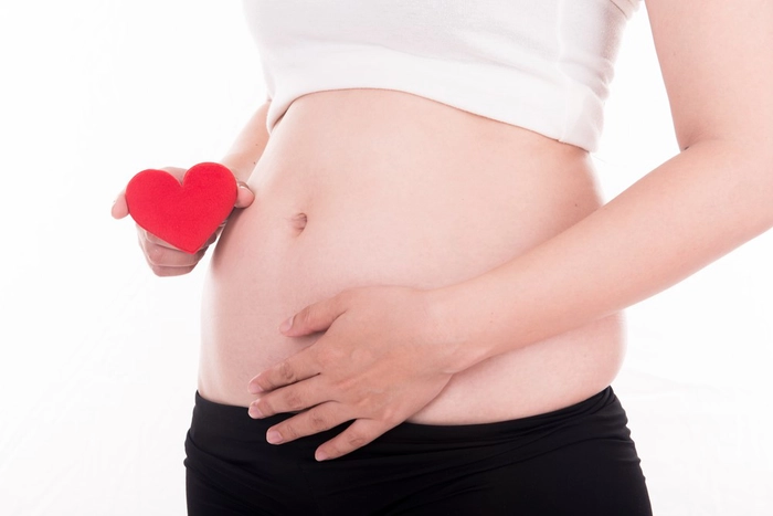 femeie insarcinata care se tine de burta si tine o inima in cealalta mana