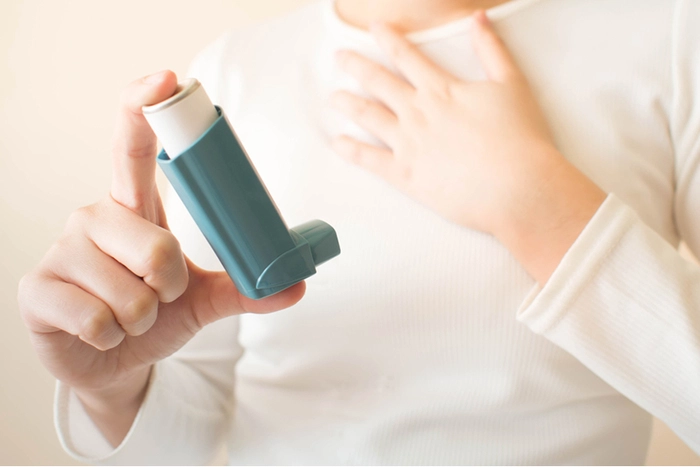 barbat care tine in mana un inhalator tinandu-se de piept