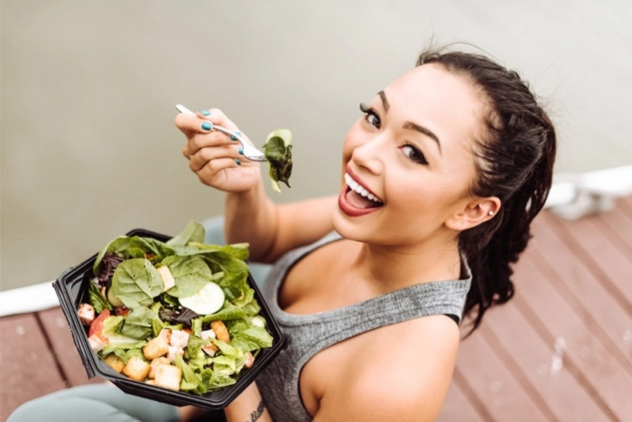 femeie care tine in mana un bol cu salata si mananca din acesta zambind