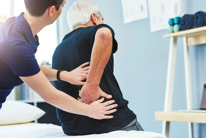barbat care face un masaj de reabilitarea unui batran care sufera de un nerv sciatic blocat