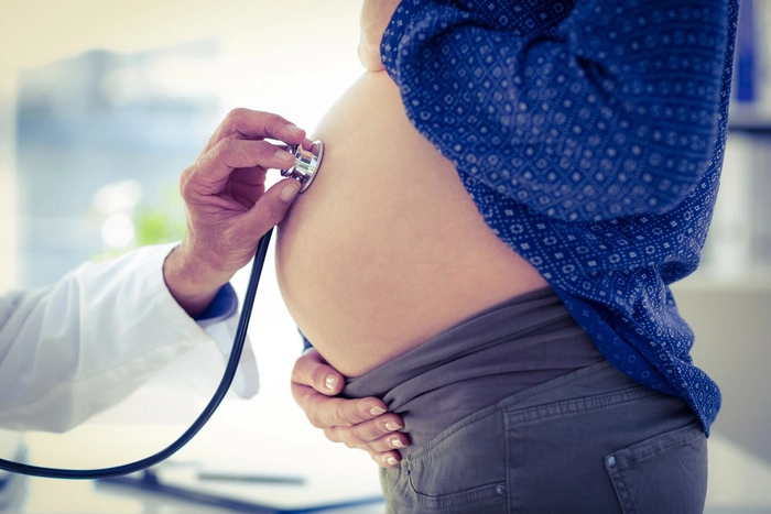 medic care asculta cu un stetoscop burta unei femei insarcinate