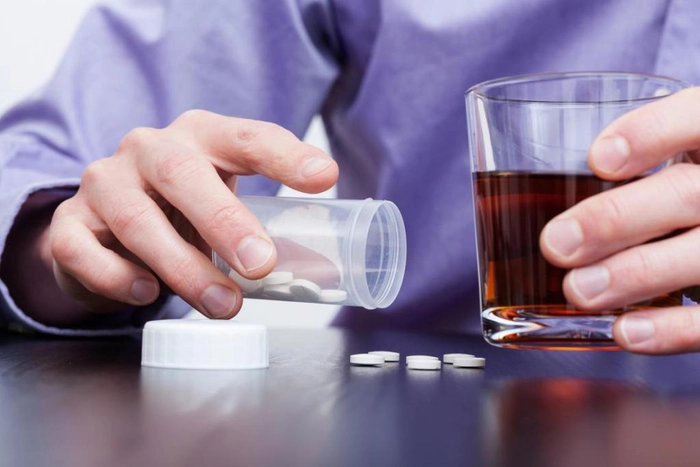 barbat care vrea sa administreze pastile tinand un pahar cu alcool 