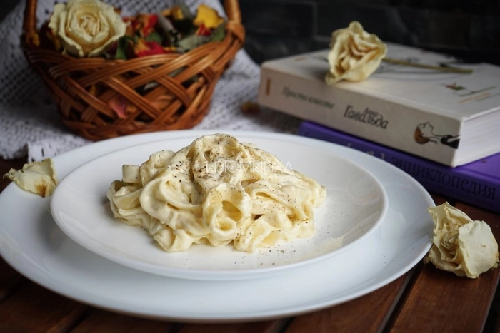 paste cu sos alfredo intr-o farfurie langa un cos si o carte pe o masa