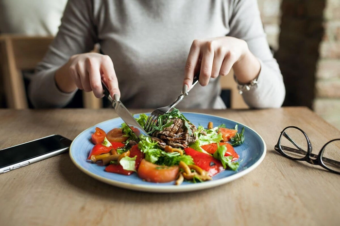 femeie care mananca o salata si are alaturi ochelari de vedere si telefonul