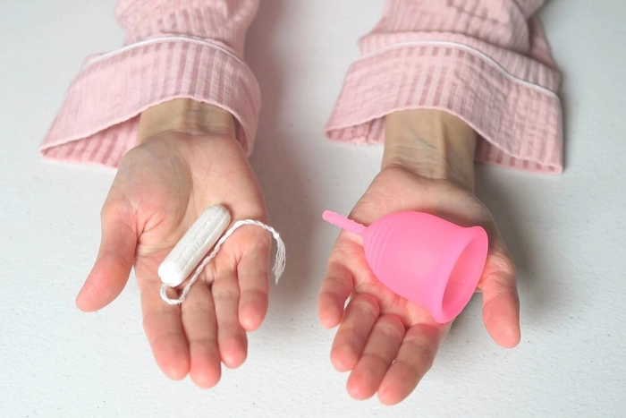 femeie care tine in mana o cupa menstruala si in alta tampoane