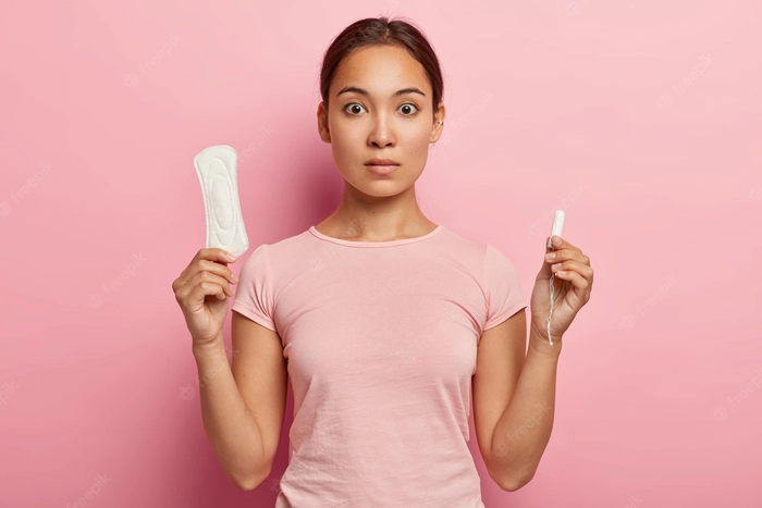 femeie care tine intr-o mana un absorbant si in alta un tampon pentru perioada ciclului menstrual