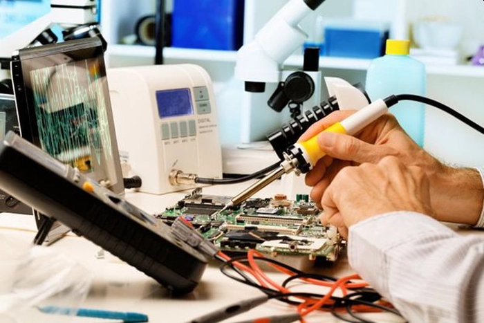o persoana intr-un laborator care tine in mana un instrument pe niste circuite