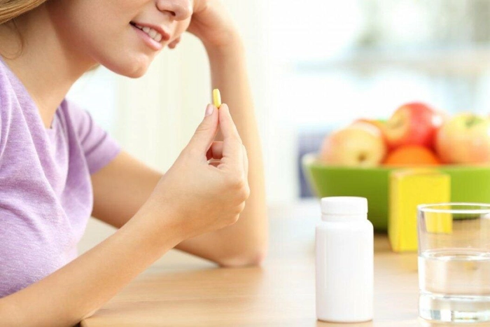 femeie care administreaza un supliment alimentar avand un recipient pe masa langa un bol cu fructe