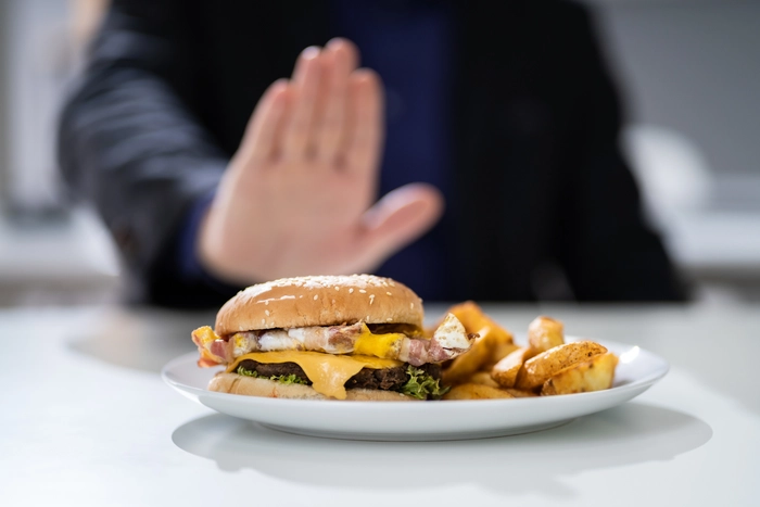 barbat care impinge o farfurie cu cartofi pai si burger