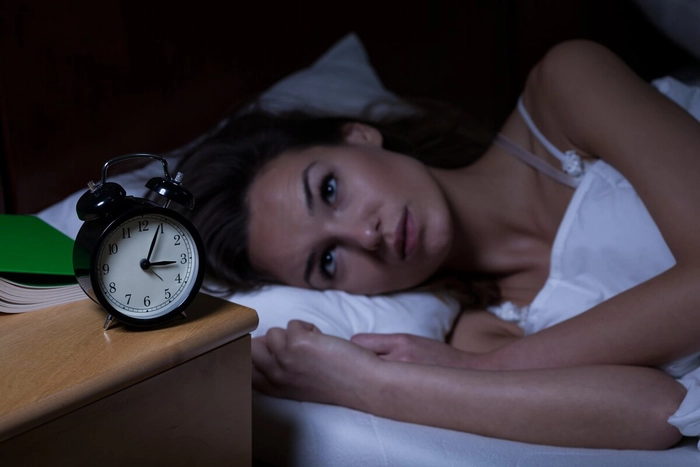 femeie care sta culcata in pat noaptea si priveste la ceas suferind de insomnie