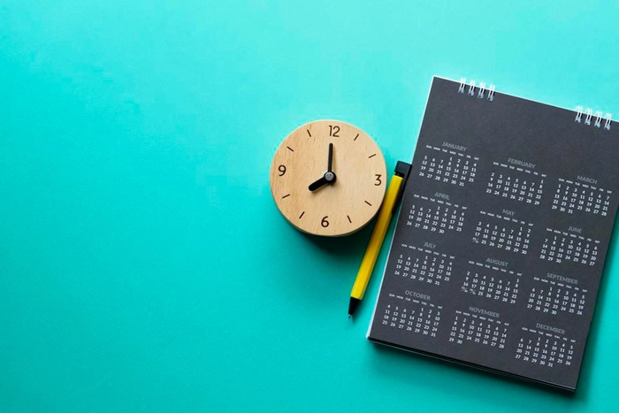 un calendar langa un creion si un ceas pe o masa