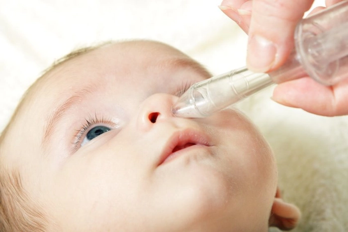 persoana care administreaza un medicament in nasul unui bebelus