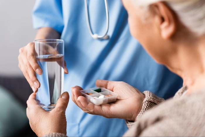un asistent medical care ajută o bătrână să consume apă și medicamente