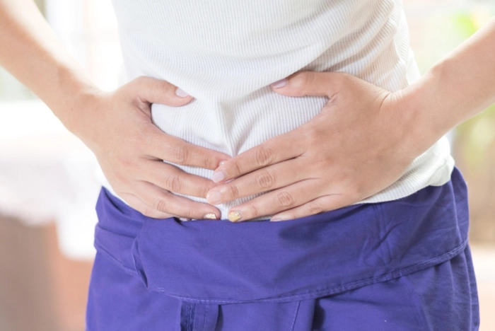 o femeie cu bluză albă și pantaloni mov care are durere de burtă