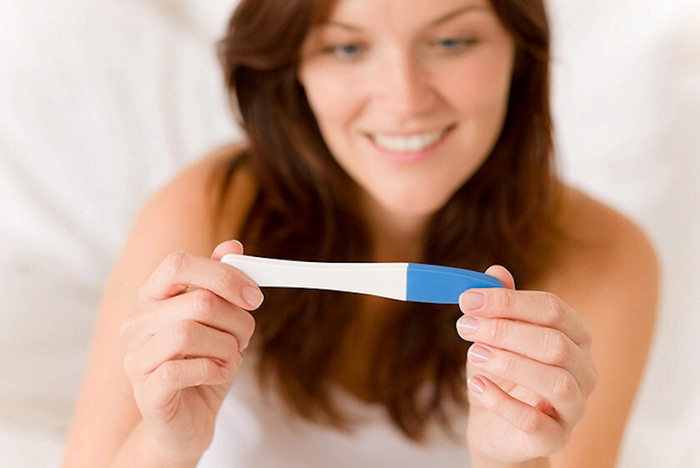 femeie care priveste un test de sarcina si zambeste