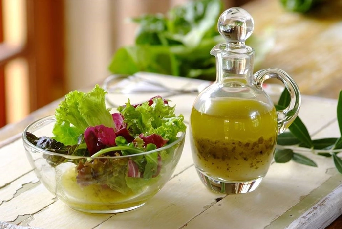 un recipient pe o masa cu sos vinegrette langa un bol cu salata