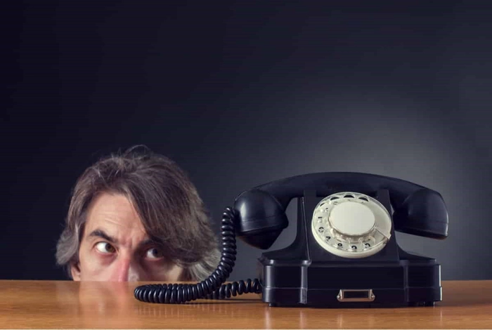 Capul unei persoane ce priveste suspicios un telefon fix  de pe o masa