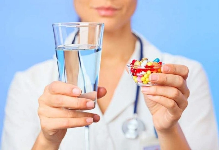 medic care tine un recipient cu pastile in mana si un pahar cu apa