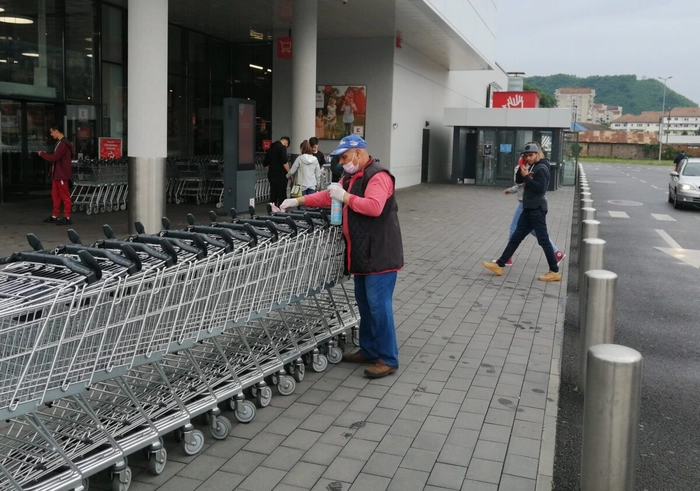 Un barbat curata carucioarele din fata unui supermarket, pe timp de zi