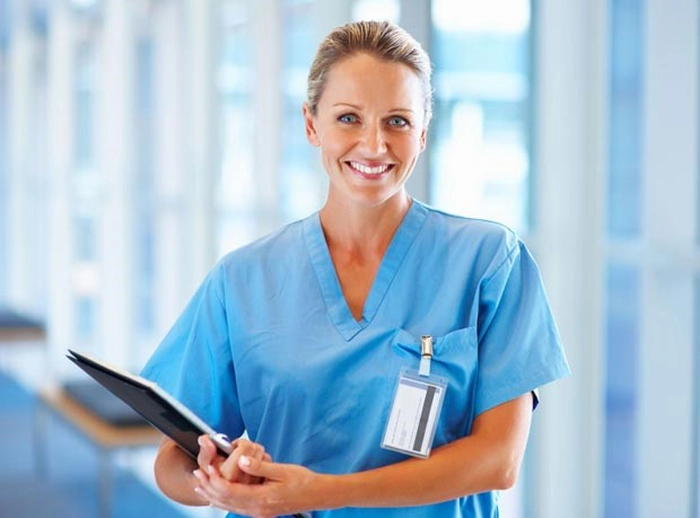  o asistenta medicala, imbracata în compleu albastru, care zambeste