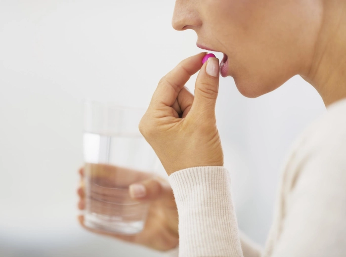 femeie care tine in mana un pahar de apa si vrea sa ia o vitamina