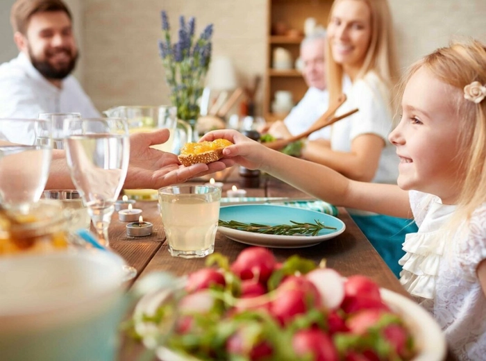o fetita care zambeste si sta la masa inconjurata de familie