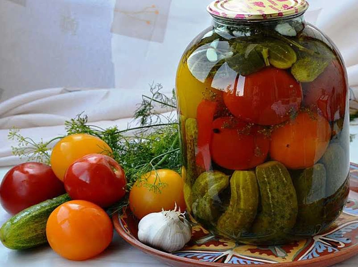 un borcan de muraturi asortate langa mai multe legume proaspete pe o masa